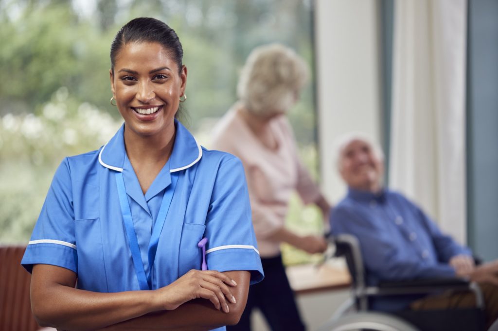 Portrait Of Female Nurse Or Care Worker Making Home Visit To Senior Couple With Man In Wheelchair